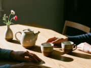 Amore ai tempi dello smartphone: come salvare la relazione dal phubbing Mani che si sfiorano su un tavolo di legno minimalista con tè caldo e luce solare calda, atmosfera intima e senza telefoni.