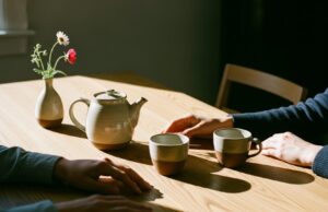 Amore ai tempi dello smartphone: come salvare la relazione dal phubbing Mani che si sfiorano su un tavolo di legno minimalista con tè caldo e luce solare calda, atmosfera intima e senza telefoni.