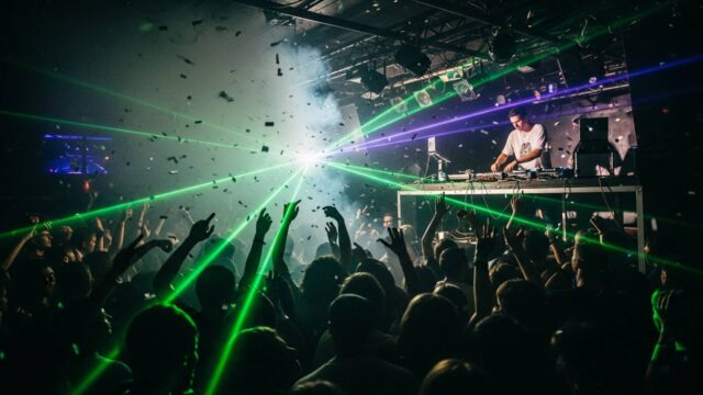 Folla in delirio balla musica dance anni 90 in discoteca con DJ set e laser verdi