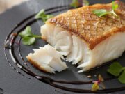 Il secondo elegante da chef: come cuocere il Baccalà in padella per una cena sofisticata Filetto di baccalà dorato cotto in padella, impiattamento elegante su piatto scuro con salsa e verdure.