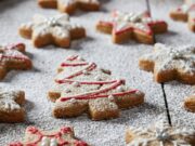 Biscotti di Natale veloci: l’impasto gluten-free a prova di principiante Biscotti di Natale veloci e fragranti senza glutine, glassati e decorati con forme festive, disposti su un piatto rustico.
