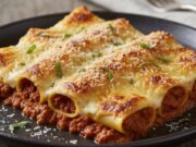 I cannelloni del giorno dopo: come riciclare il ragù avanzato in un primo piatto da gourmet Cannelloni al forno gratinati con besciamella e ragù, fumanti e pronti da gustare su piatto rustico.