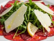 Antipasto di Capodanno elegante in 5 minuti: il carpaccio di bresaola gourmet che non richiede cottura Fette sottili di carpaccio di bresaola condite con scaglie di parmigiano, rucola e dressing, antipasto gourmet elegante.