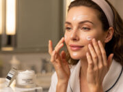 Crema notte all’acido ialuronico: perché fa la differenza Applicazione di crema viso idratante notte: donna che stende il prodotto su guance e fronte con barattolo di acido ialuronico in primo piano