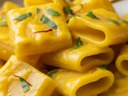 Primo piatto per il pranzo di Capodanno: i paccheri cremosi allo zafferano pronti in 20 minuti paccheri cremosi zafferano, primo piatto ricco e giallo brillante, servito con prezzemolo fresco su tavolo rustico.