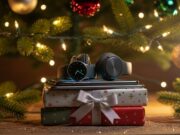 I regali tech sotto l’albero: la top 5 dei gadget più desiderati per questo natale Illustrazione festiva di una pila di gadget tech (smartphone, smartwatch, cuffie) impacchettati sotto un albero di Natale illuminato.