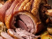 Stinco di maiale alla Bavarese: l’antica tecnica della doppia cottura per una carne che si scioglie Stinco di maiale bavarese intero, cotto al forno, con pelle croccante e lucida, su piatto di ceramica scura.