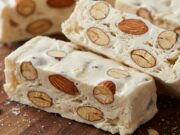 Il torrone fatto in casa: i trucchi per montare l’albume senza fatica Fette di torrone bianco lucido fatto in casa con mandorle intere su tagliere rustico.
