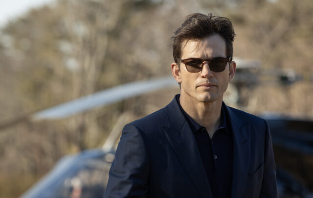 Ashton Kutcher con occhiali da sole e abito scuro in una scena della serie TV The Beauty di Disney+