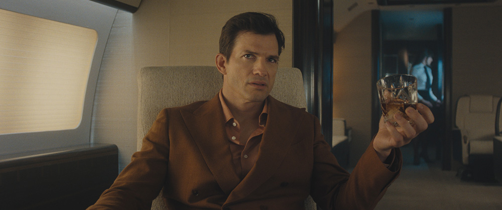 Ashton Kutcher interpreta un miliardario in una scena della serie Disney+ The Beauty mentre tiene un bicchiere di whisky.