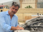 Convertini presenta il libro «Il paese delle tradizioni» a Martina Franca Beppe Convertini in posa appoggiato a un'antica imbarcazione in legno con sfondo architettonico.