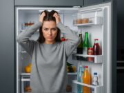 Dieta post-feste: i 7 errori da evitare per non vanificare gli sforzi della depurazione Donna che si tocca la testa frustrata davanti al frigorifero, simboleggiando gli errori comuni nella dieta post-feste.