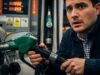 Hai messo Benzina nel Diesel? Non girare la chiave: l’errore che ti brucia il motore. Primo piano su un automobilista confuso e agitato mentre realizza di aver inserito l'ugello sbagliato (diesel o benzina) nel serbatoio del veicolo, con i display della pompa di benzina sullo sfondo.