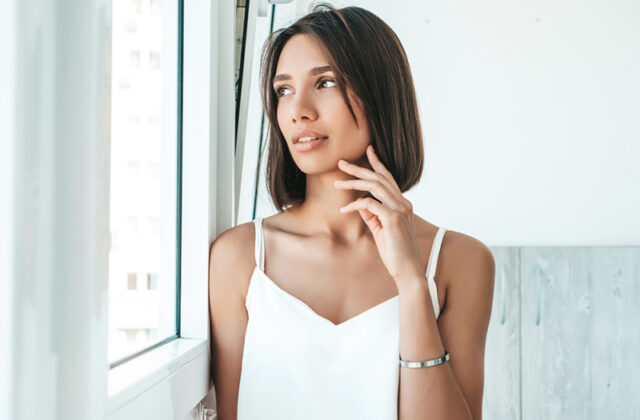 Donna con top bianco che indossa un bracciale rigido in argento vicino a una finestra