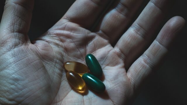 Mano che regge integratori alimentari naturali e capsule in gel, simbolo dei rischi e delle interazioni epatiche.