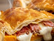 Torta salata con zucca, speck e scamorza: la ricetta veloce pronta in 30 minuti Fetta di torta salata con zucca, speck croccante e scamorza filante su tagliere di legno. pronto da mangiare.