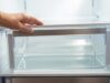 Acqua sotto i cassetti del frigorifero: come liberare il foro di scolo e salvare il compressore Pozzanghera d'acqua trasparente sotto il cassetto della verdura di un frigorifero aperto da una mano.