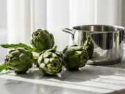 Perché i carciofi anneriscono in cottura: la reazione chimica con le pentole Carciofi freschi su un piano in marmo accanto a una pentola in acciaio inossidabile
