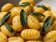 Gnocchi di patate talmente soffici che si sciolgono in bocca, con burro e salvia croccante Gnocchi di patate freschi serviti in un piatto di ceramica con abbondante burro fuso dorato e foglie di salvia croccante.