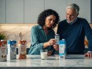 Latte vegetale tossico? Svelati gli ingredienti che distruggono il metabolismo silenziosamente Coppia in cucina controlla con preoccupazione gli ingredienti sull'etichetta di una confezione di latte vegetale industriale