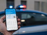 Patente Digitale su App IO: l’errore del “semplice screenshot” che può costarti una multa Primo piano di una mano che tiene uno smartphone con una patente digitale e un codice QR, con luci della polizia sfocate sullo sfondo.
