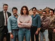 Perché la seconda stagione di Vanina cambia il volto del poliziesco italiano Giusy Buscemi, nei panni della vicequestore Vanina Guarrasi, posa al centro a braccia conserte circondata dalla sua squadra investigativa sui tetti di Catania, sotto un cielo plumbeo.