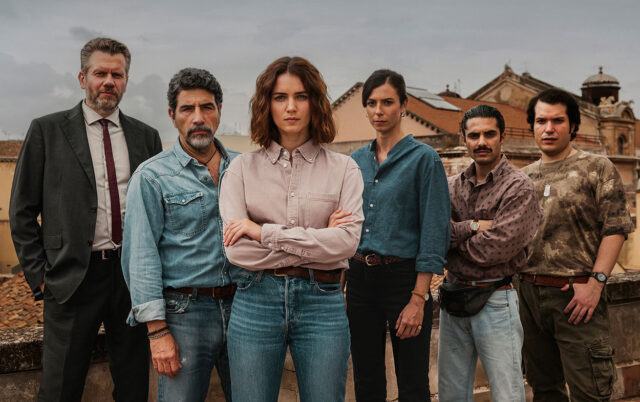 Giusy Buscemi, nei panni della vicequestore Vanina Guarrasi, posa al centro a braccia conserte circondata dalla sua squadra investigativa sui tetti di Catania, sotto un cielo plumbeo.