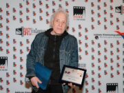 Il trionfo dello sguardo femminile al BAFF: cronaca di un festival che guarda al futuro Il regista Abel Ferrara posa con il Premio Dino Ceccuzzi all'eccellenza cinematografica davanti al backdrop ufficiale del B.A. Film Festival.