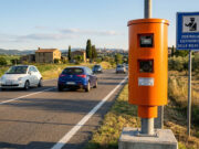 Multe autovelox 2026: i dispositivi illegali da maggio e come leggere il verbale Autovelox a colonnina arancione su una strada extraurbana italiana con cartello blu di controllo elettronico della velocità e auto in transito