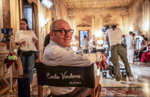 Carlo Verdone e la sfida della fragilità in “Scuola di seduzione”, dal 1° aprile su Paramount + Carlo Verdone sul set del film "Scuola di seduzione" seduto sulla sedia da regista personalizzata in un interno d'epoca.