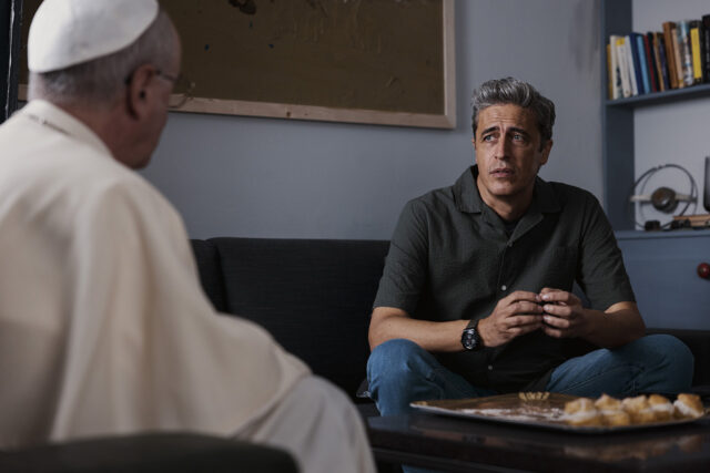 Il protagonista Arturo, interpretato da Pif, è seduto su un divano e conversa con espressione intensa e preoccupata con il Papa, che appare di spalle in primo piano. Sul tavolino davanti a loro è posizionato un vassoio di dolci tipici della pasticceria siciliana.