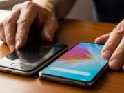 Come trasferire le app sul nuovo smartphone senza bloccare il telefono o perdere dati Dettaglio delle mani di un uomo maturo che appoggia un vecchio smartphone accanto a un telefono nuovo su una scrivania di legno.