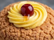 Zeppole di San Giuseppe in friggitrice ad aria: la tecnica per non farle sgonfiare Dettaglio ravvicinato di una zeppola dorata e porosa farcita con crema pasticcera vellutata e un'amarena sciroppata lucida.