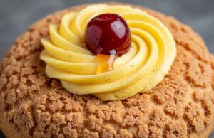 Zeppole di San Giuseppe in friggitrice ad aria: la tecnica per non farle sgonfiare Dettaglio ravvicinato di una zeppola dorata e porosa farcita con crema pasticcera vellutata e un'amarena sciroppata lucida.