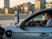 Auto ibride 2026: la guida definitiva per chi non vuole ancora l’elettrica (ma deve cambiare auto adesso) Uomo d'affari controlla l'autonomia elettrica di 85 km sulla sua auto ibrida plug-in del 2026 in una stazione di ricarica urbana al tramonto