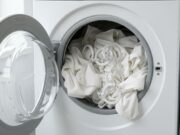 Pulizie di primavera: l’errore nel lavaggio delle tende che rovina i binari e la lavatrice Dettaglio di tende bianche caricate in lavatrice con ganci di plastica ancora attaccati, errore tipico delle pulizie di primavera che rischia di danneggia il cestello.