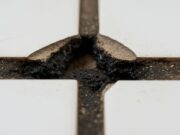 Pulizia fughe pavimenti: l’errore con la candeggina che sgretola lo stucco Primo piano macro di fughe pavimenti nere e sgretolate a causa dell'uso di candeggina e detersivi acidi corrosivi