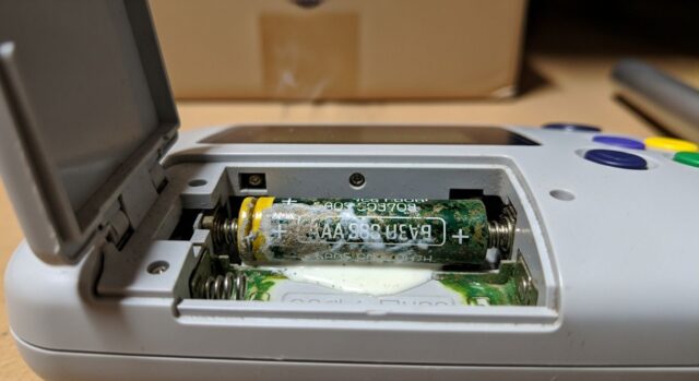 Inquadratura macro autentica della corrosione bianca e verde causata dalle vecchie pile AA nel vano batterie di un gioco elettronico portatile vintage
