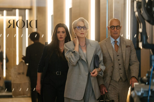 Anne Hathaway, Meryl Streep e Stanley Tucci camminano insieme in un ufficio con il logo Dior sullo sfondo, in una scena ufficiale del film Il Diavolo Veste Prada 2.