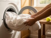 Lavare il piumone a casa: l’errore del ciclo delicato che marcisce le piume Piumone bianco pulito inserito in una lavatrice moderna con luce naturale.