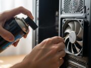 Pulizia di pc e console: l’errore con l’aspirapolvere che frigge la scheda madre Dettaglio ravvicinato di mani che usano una bomboletta ad aria compressa e uno stuzzicadenti per pulire la ventola di un computer.