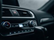 Ricircolo aria auto: l’errore in primavera che fa puzzare il climatizzatore Dettaglio del pulsante del ricircolo dell'aria acceso sulla plancia di un'automobile moderna con parabrezza appannato sullo sfondo.
