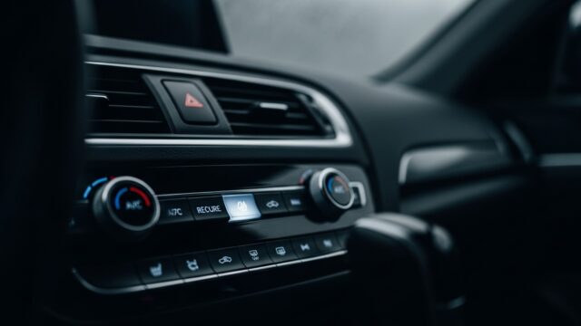 Dettaglio del pulsante del ricircolo dell'aria acceso sulla plancia di un'automobile moderna con parabrezza appannato sullo sfondo.