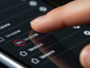 Android Auto e CarPlay si disconnettono alla guida: come risolvere il problema delle interferenze Wi-Fi Primo piano macro di un dito che esegue 10 tap sulla voce Versione nelle impostazioni per sbloccare il menu segreto sviluppatore e risolvere i crash wireless.