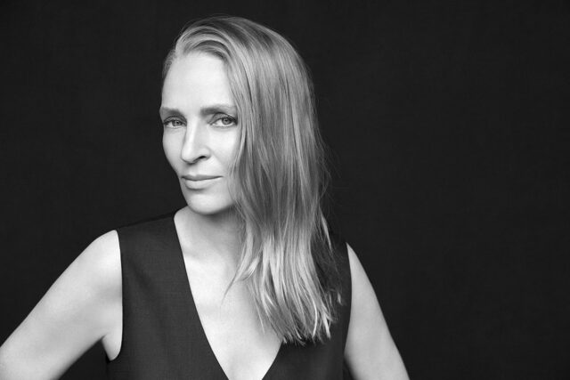 Ritratto fotografico in bianco e nero dell'attrice Uma Thurman in posa frontale su sfondo scuro.