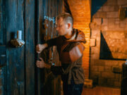 Intrattenimento immersivo: come le escape room stanno cambiando il tempo libero nelle grandi città Un uomo impegnato a risolvere un enigma davanti a una porta di legno in una escape room a tema medievale.