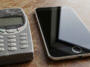Perché i ventenni stanno buttando gli smartphone per tornare ai vecchi Nokia a tasti Vecchio cellulare Nokia a tasti usurato a confronto con uno smartphone moderno sul tavolo, simbolo del trend digital detox e dumbphone