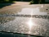 Lavare l’auto al sole opacizza la vernice: l’errore del pomeriggio estivo Dettaglio dei danni al trasparente e aloni di calcare sul cofano rovente di una vettura estiva.