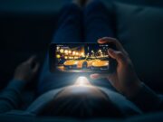 Zeus di Monaco: perché milioni di italiani seguono un avvocato parigino in Lamborghini Persona sdraiata sul divano che osserva uno smartphone con immagini di supercar di lusso illuminato nell'oscurità