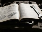 Manutenzione auto fai da te: gli errori che annullano la garanzia senza che tu lo sappia Manuale d'uso e manutenzione aperto e appoggiato su un motore polveroso all'interno di un'officina.